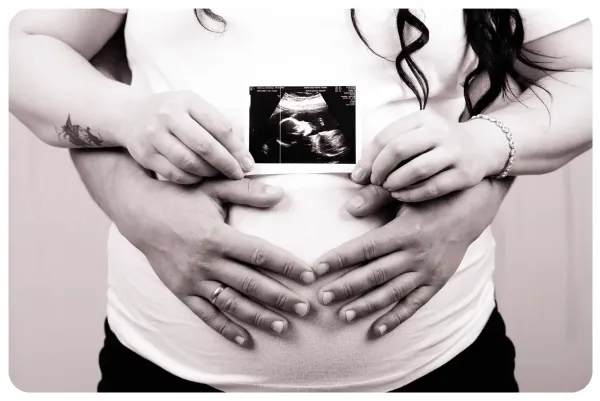 Black and white maternity photograph with hands and an ultrasound picture