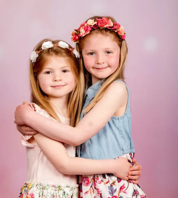 Two children embracing in front of a pink studio backdrop